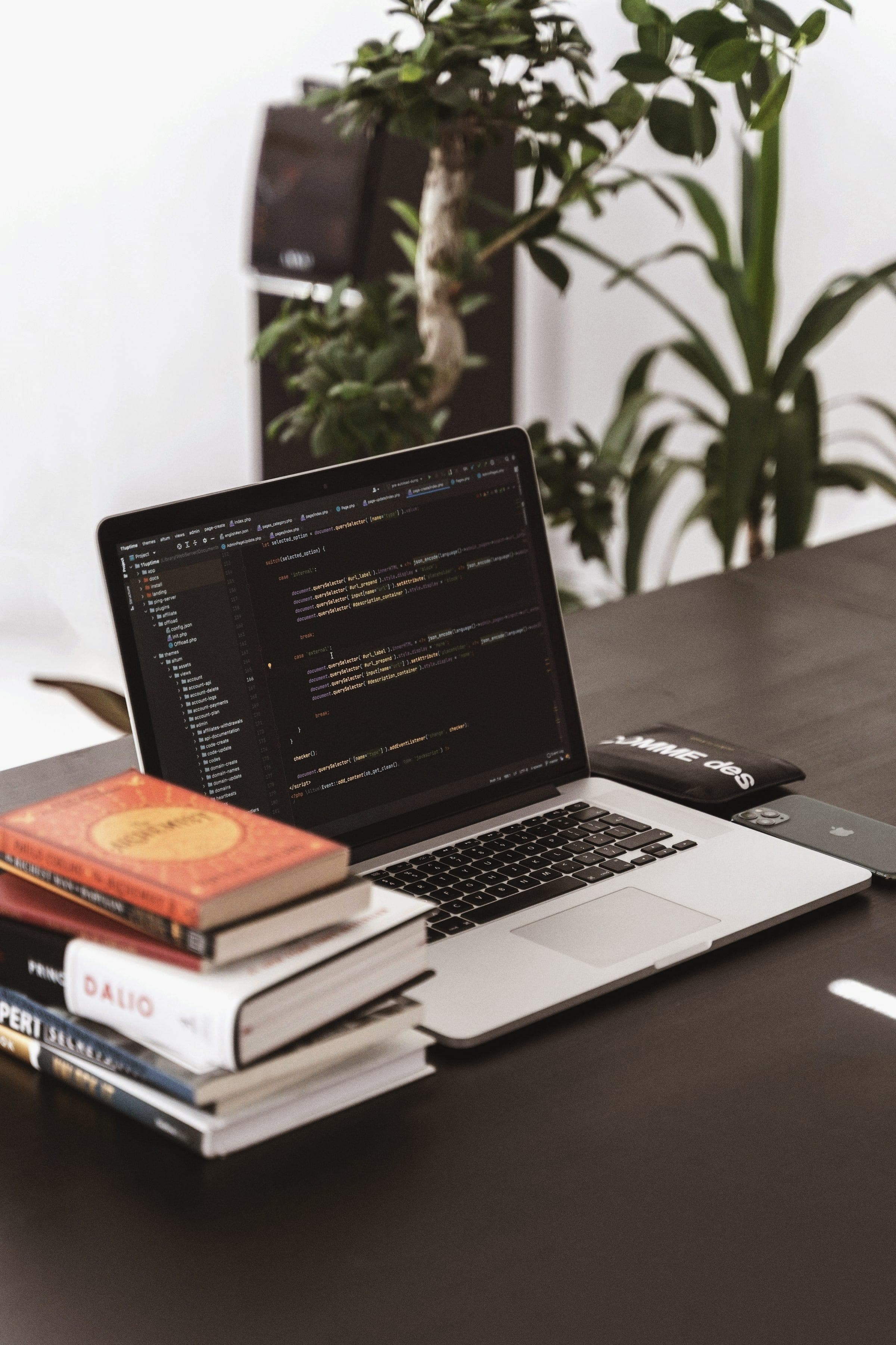 A laptop showing code on a desk beside a stack of books